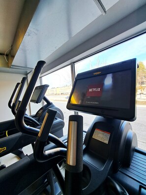 Un gimnasio con cintas de correr y una pantalla digital que muestra 'NETFLIX'.
