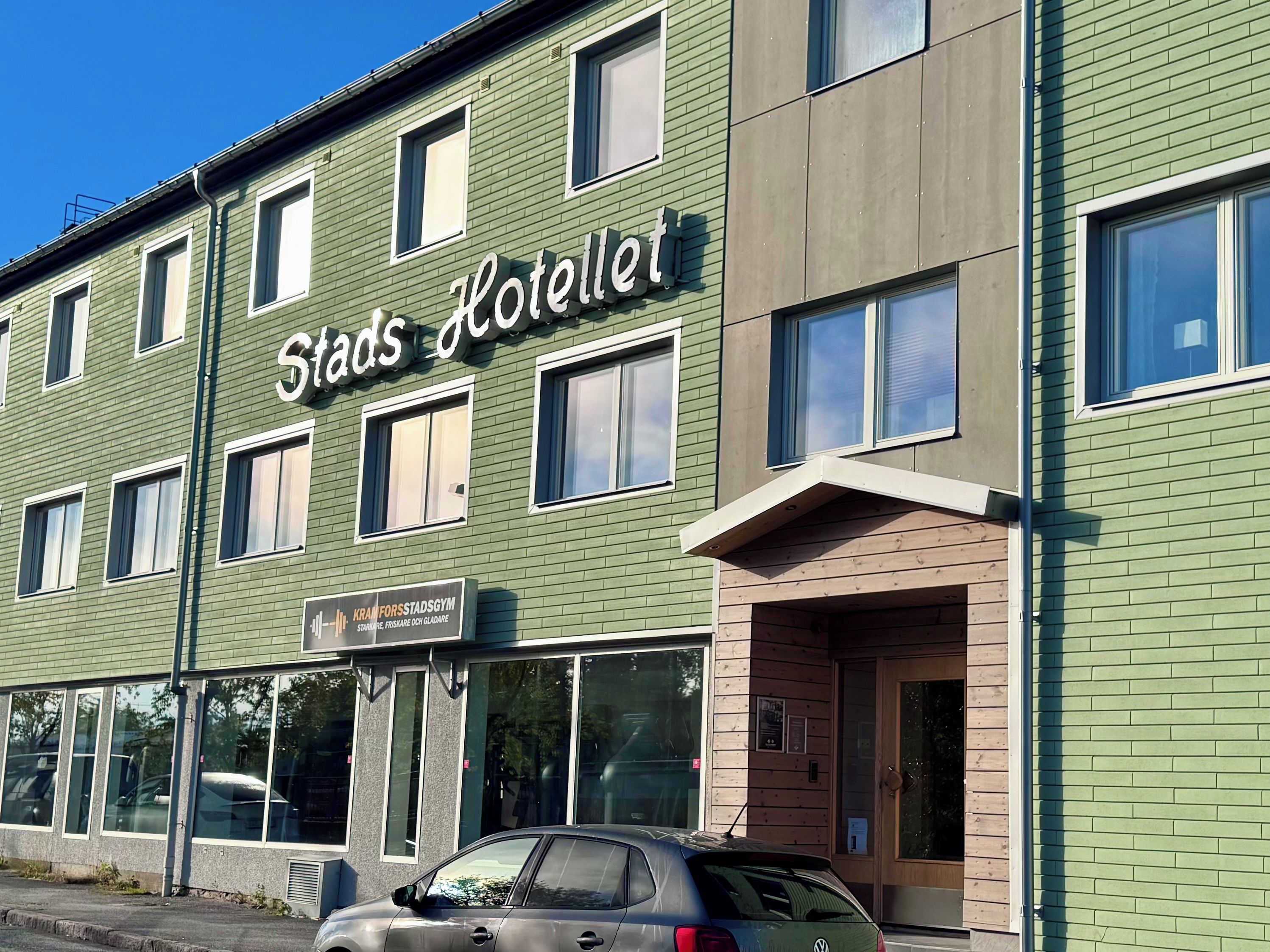 En byggnad med flera våningar, med en skylt som visar texten ”Stads Hotellet” och en skylt för ett gym under.