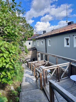Une terrasse en bois menant à un bâtiment doté de nombreuses fenêtres et d’un toit en métal.