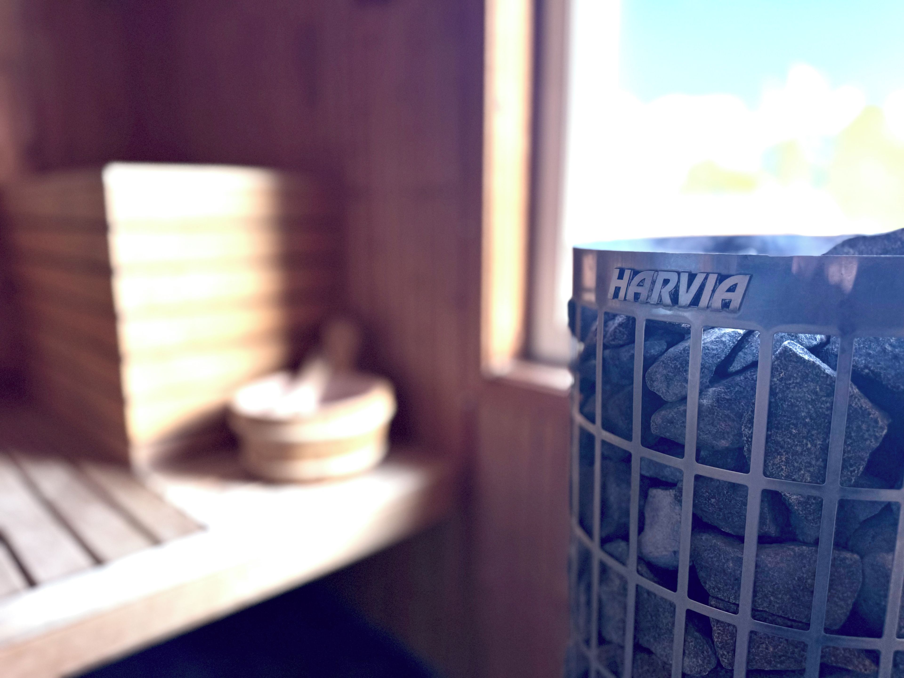 Una ventana con vista a un edificio y un contenedor de basura con la etiqueta 'HARVIA' y piedras en su interior.