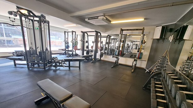 Un gimnasio con diversos equipos de ejercicio, incluyendo bancos, jaulas para pesas y pesas sueltas.