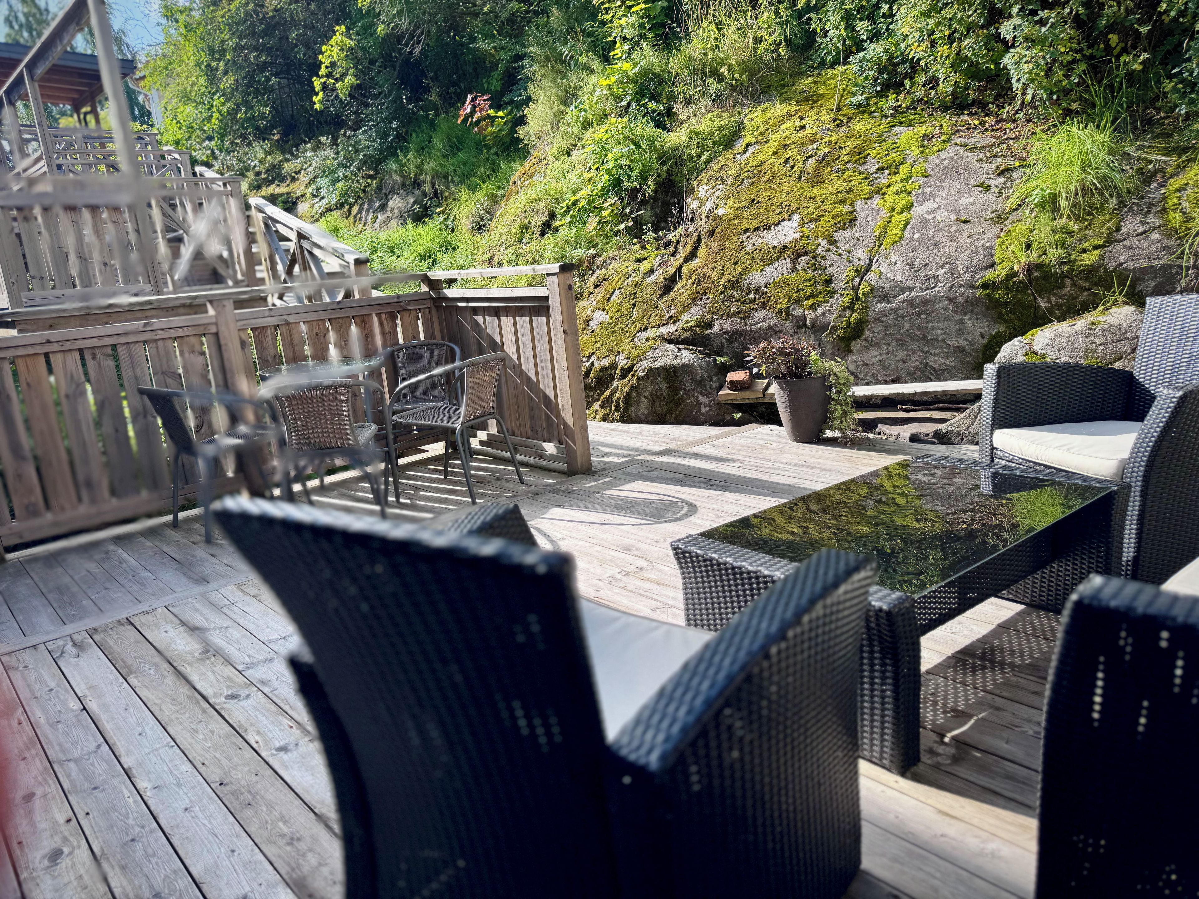 Terraza exterior con mobiliario de mimbre, una mesa de madera y una pared de roca cubierta de musgo.