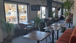 Un espacio interior amplio con mesas y sillas, ventanas grandes y plantas en macetas.