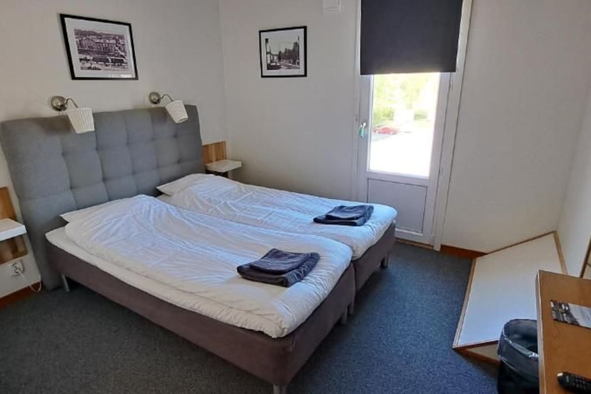 Una habitación con cama doble, mesitas de noche, un escritorio con silla y una ventana.