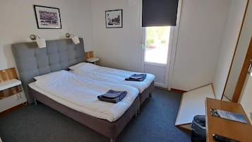 Una habitación con cama doble, mesitas de noche, un escritorio con silla y una ventana.
