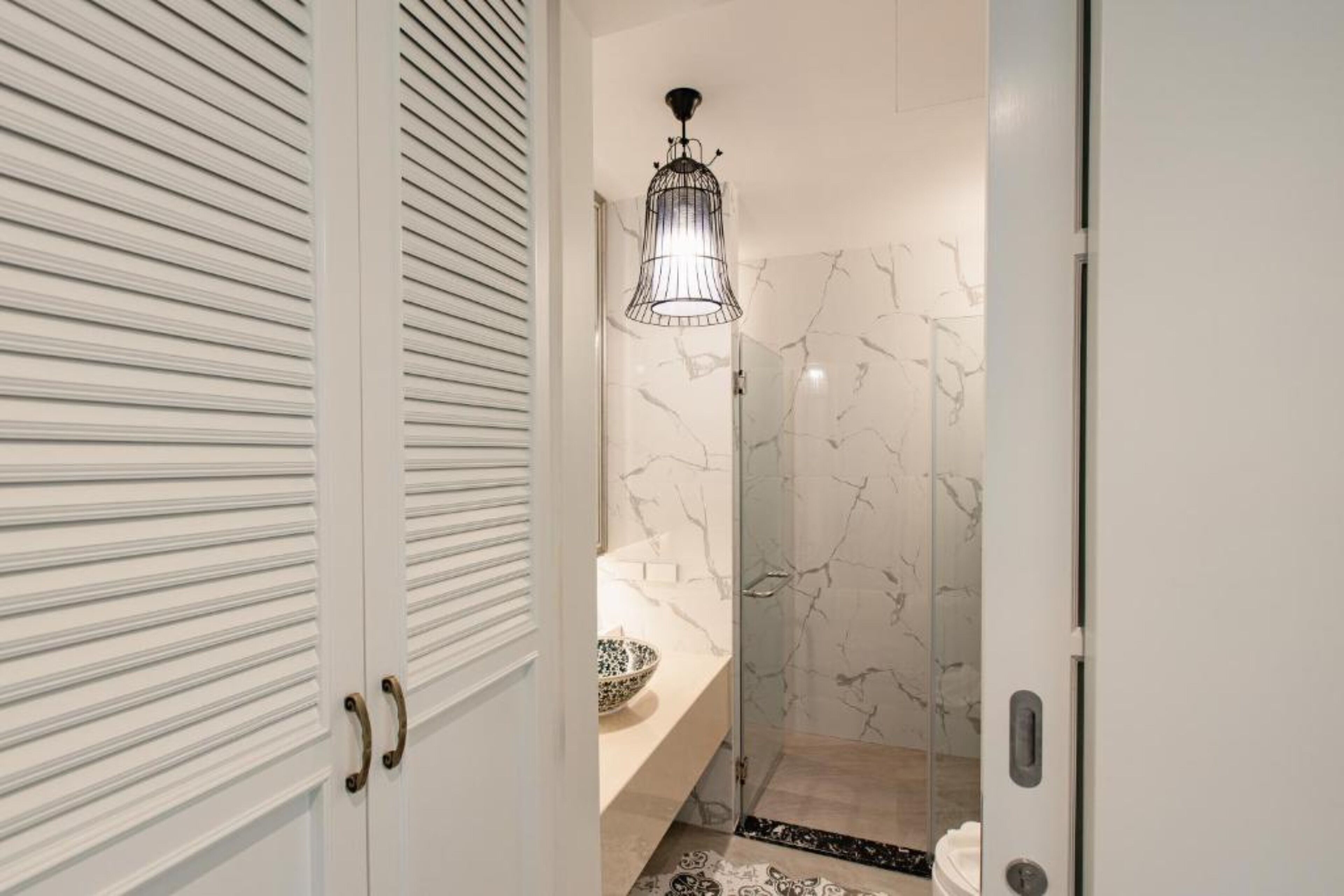 A bathroom with a marble wall, a glass shower enclosure, and a pendant light.
