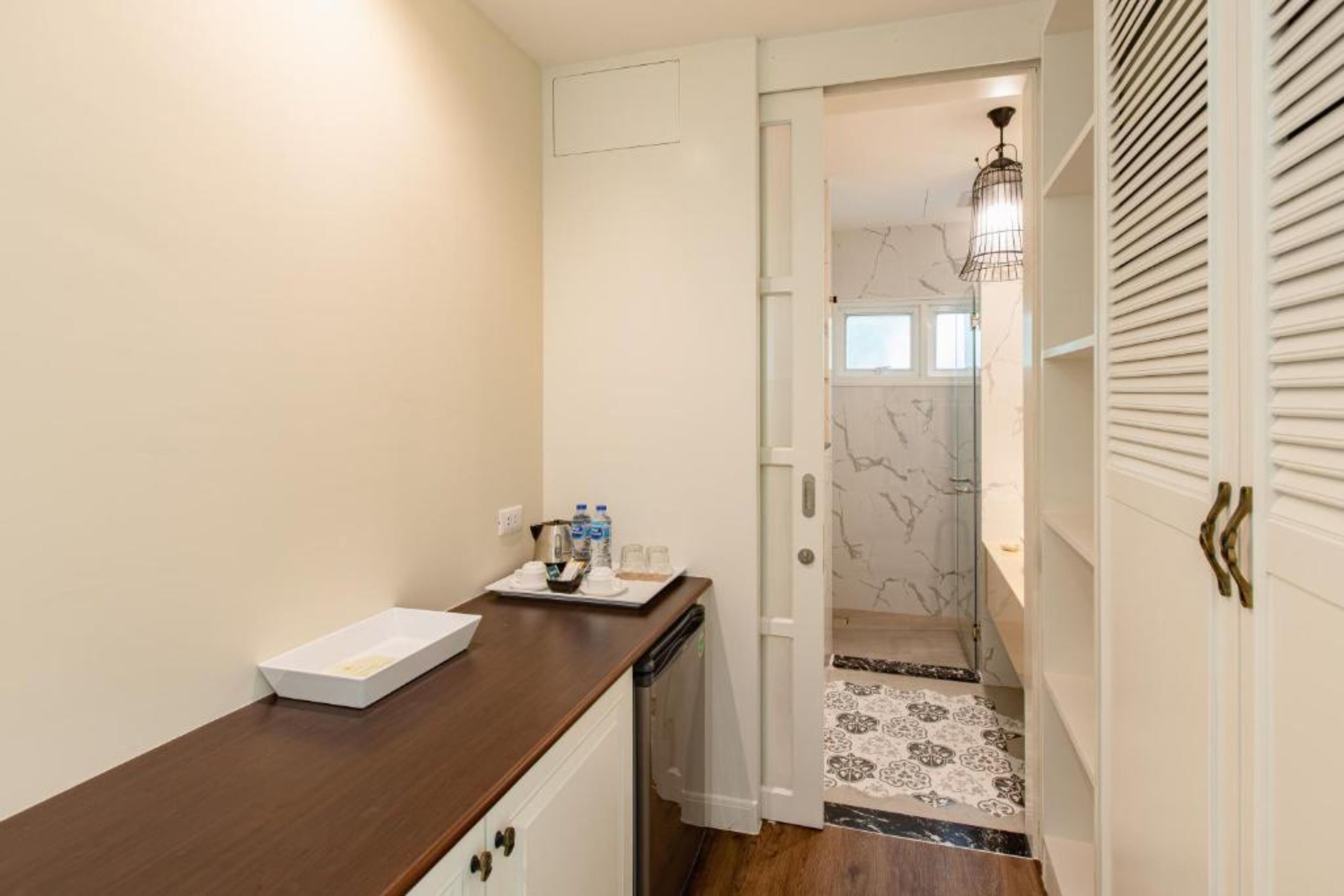 Un couloir étroit avec un comptoir en bois, un petit lavabo et une porte donnant sur une salle de bain équipée d’une douche en marbre.