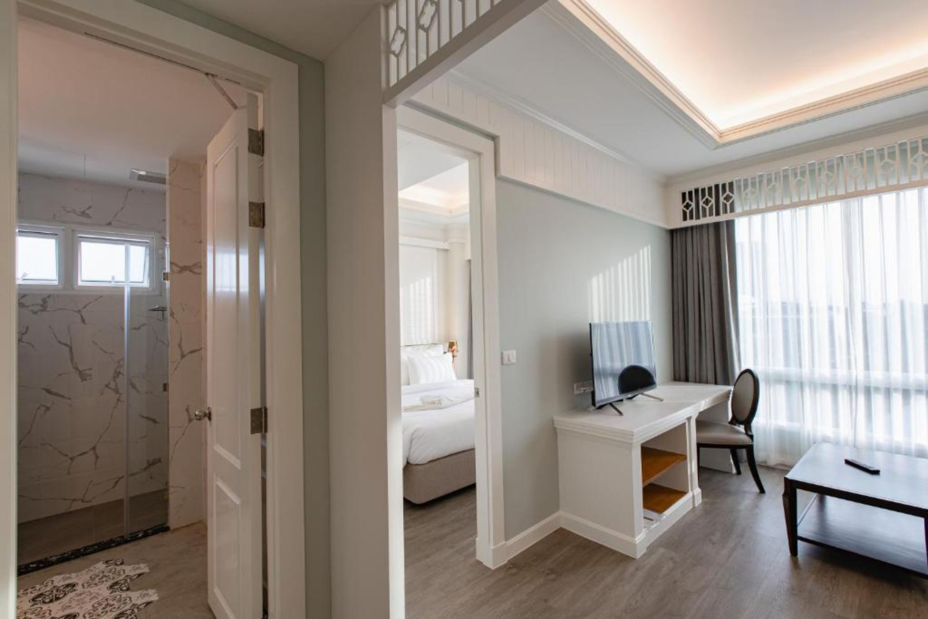 Een hotelkamer met een bed, bureau, stoel, televisie en raam met gordijnen.