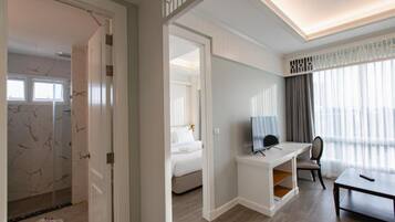 Ett hotellrum med en säng, ett skrivbord, en stol, en tv och ett fönster med gardiner.