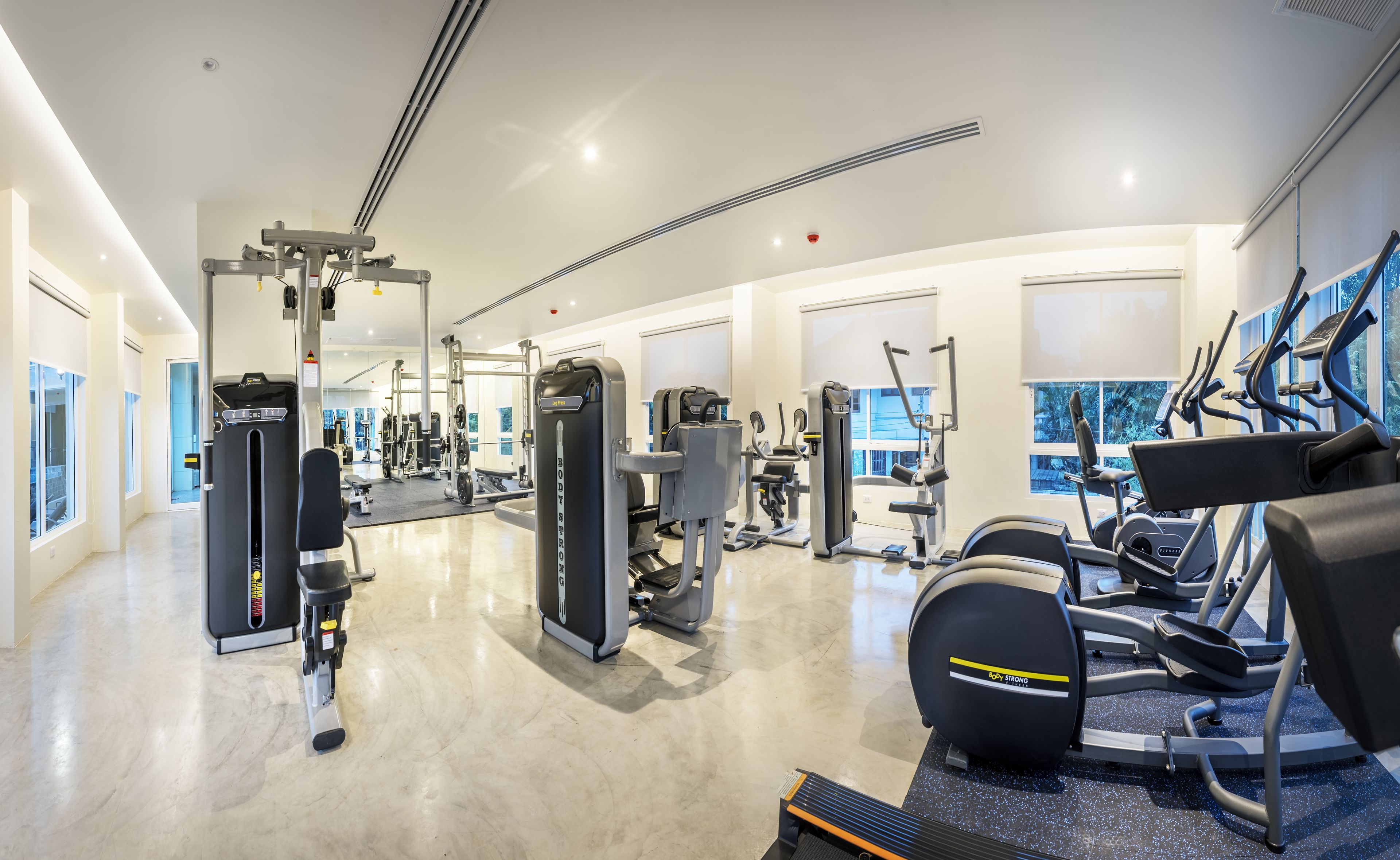 A modern gym with various exercise equipment, large windows, and a clean, spacious layout.