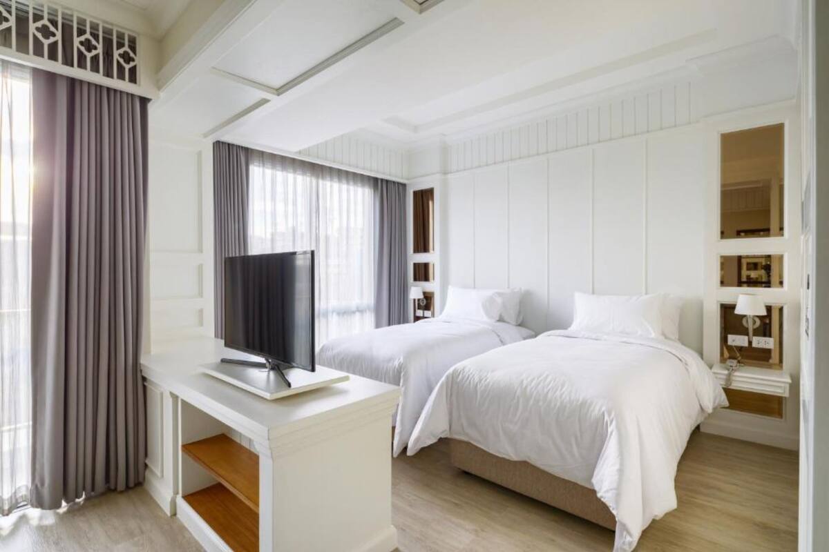 A hotel room with two beds, a desk with a TV, and a window with curtains.