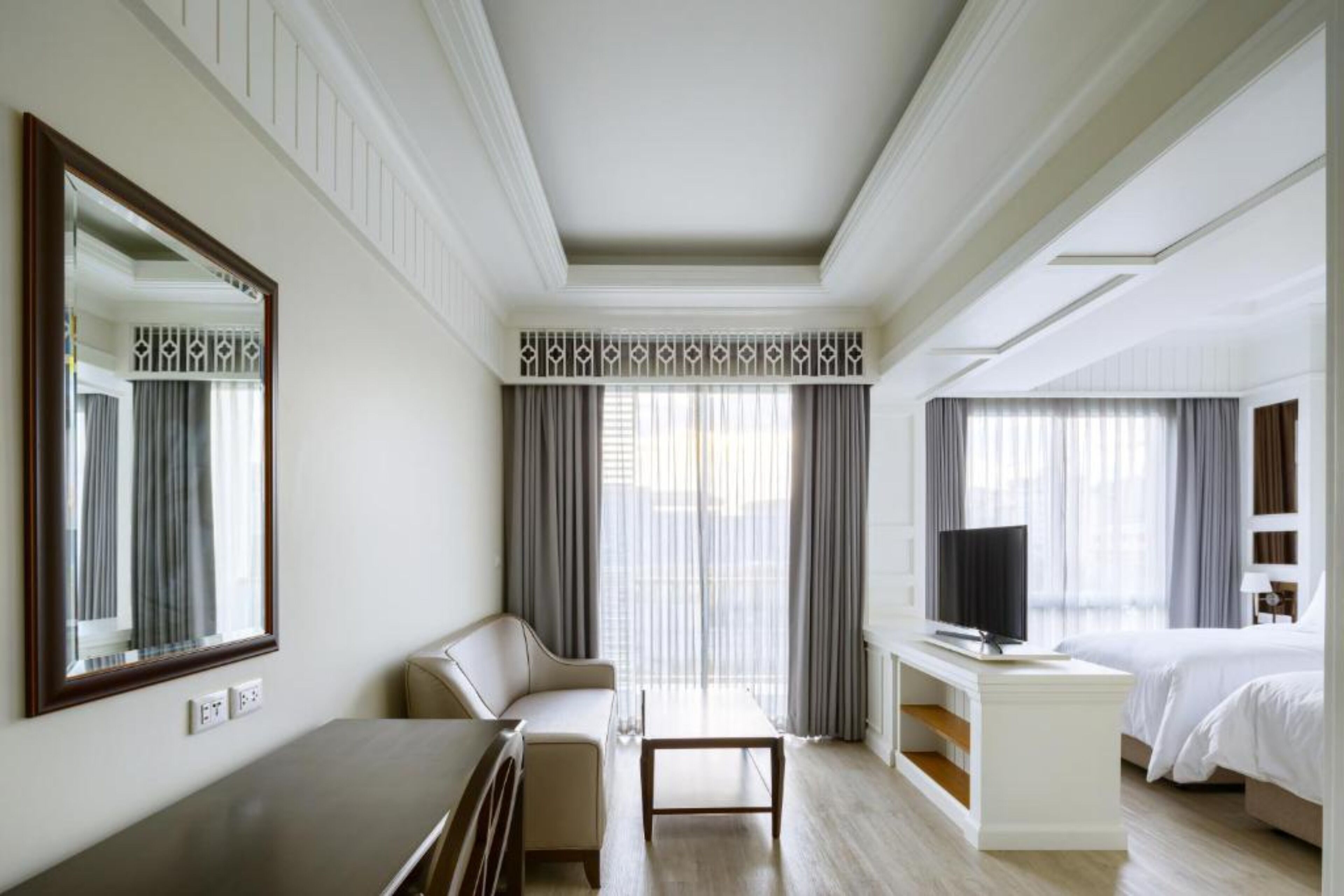 A hotel room with a large bed, a TV, a sofa, a desk, and a large mirror.