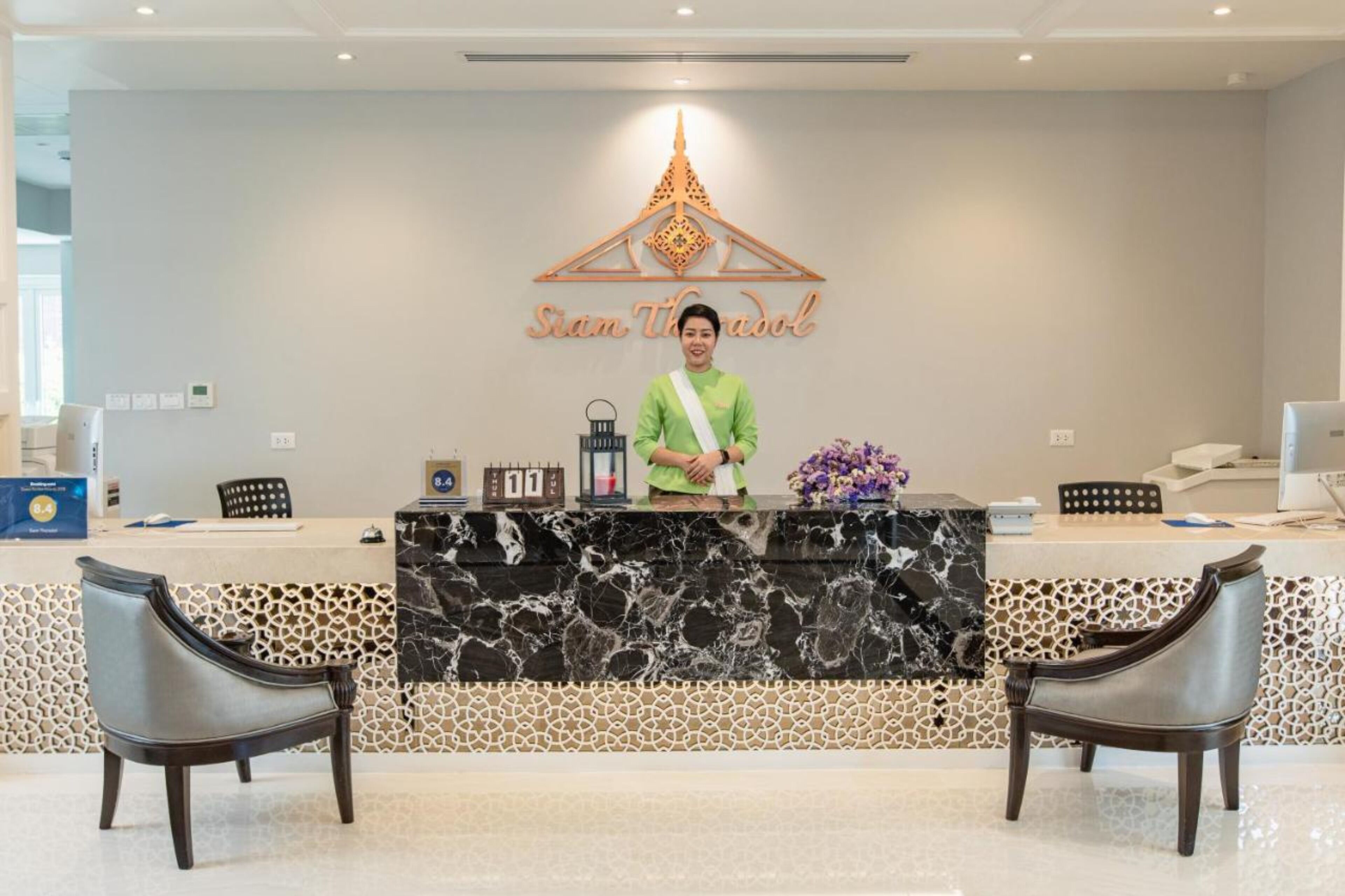A reception desk with a marble top, two chairs, a wall clock, and a decorative wall piece.