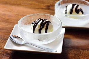 Dos tazones de helado con goteado de chocolate sobre una mesa de madera.