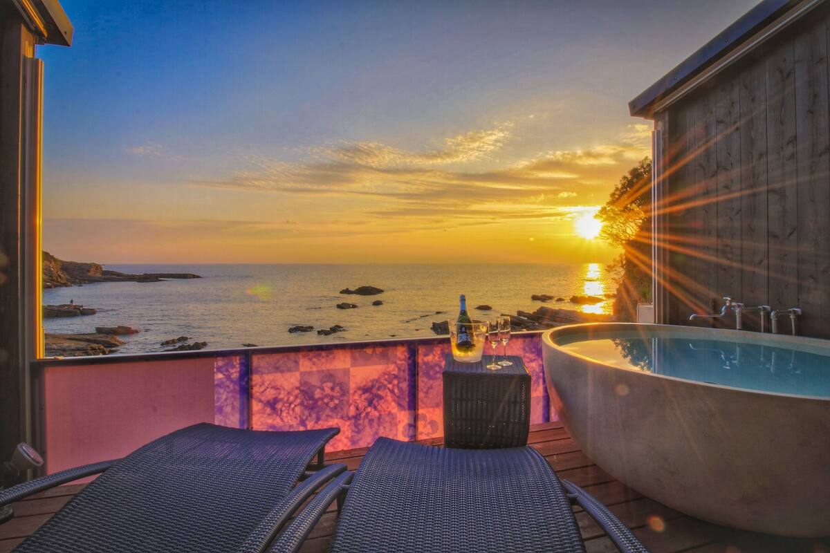 A sunset view from a balcony with a pool and lounge chairs.