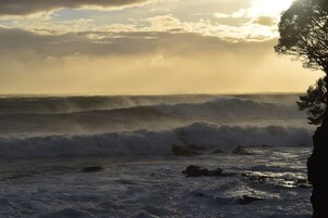 Paisaje costero con olas rompiendo contra rocas bajo un cielo nublado.