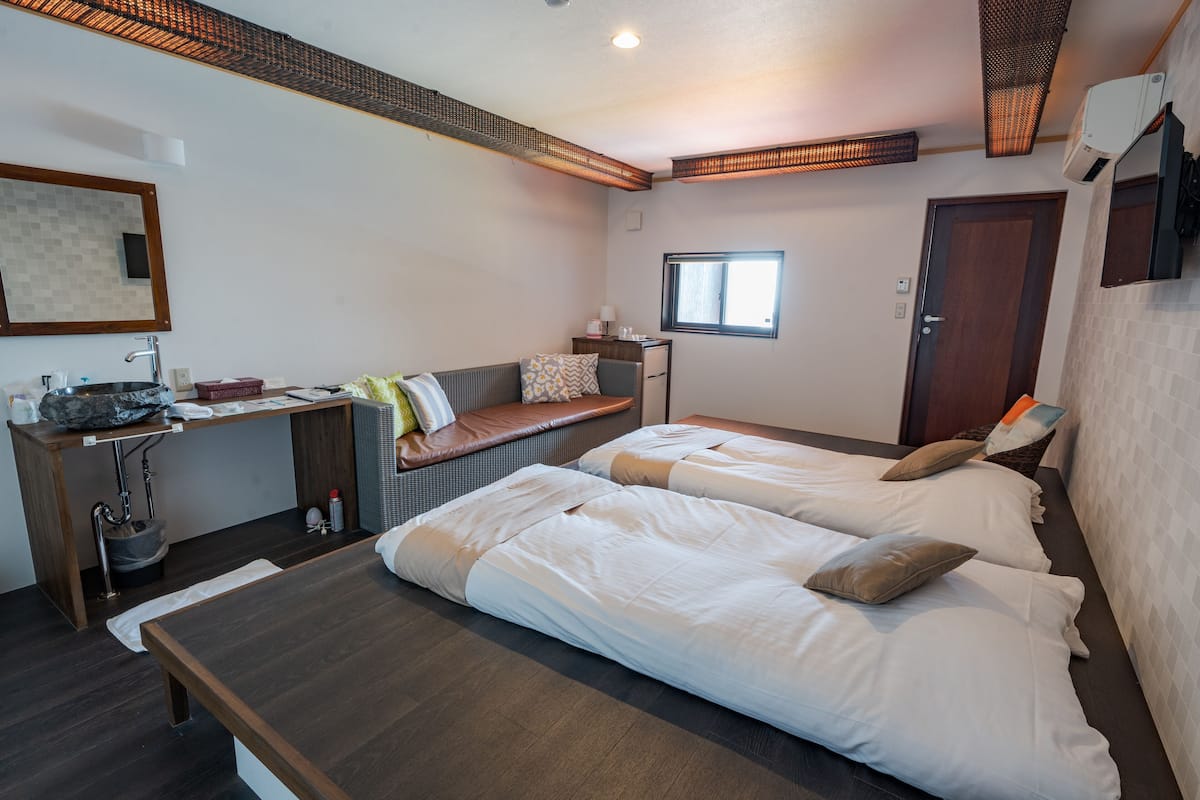 A modern hotel room with two beds, a desk, a window, and a bathroom.