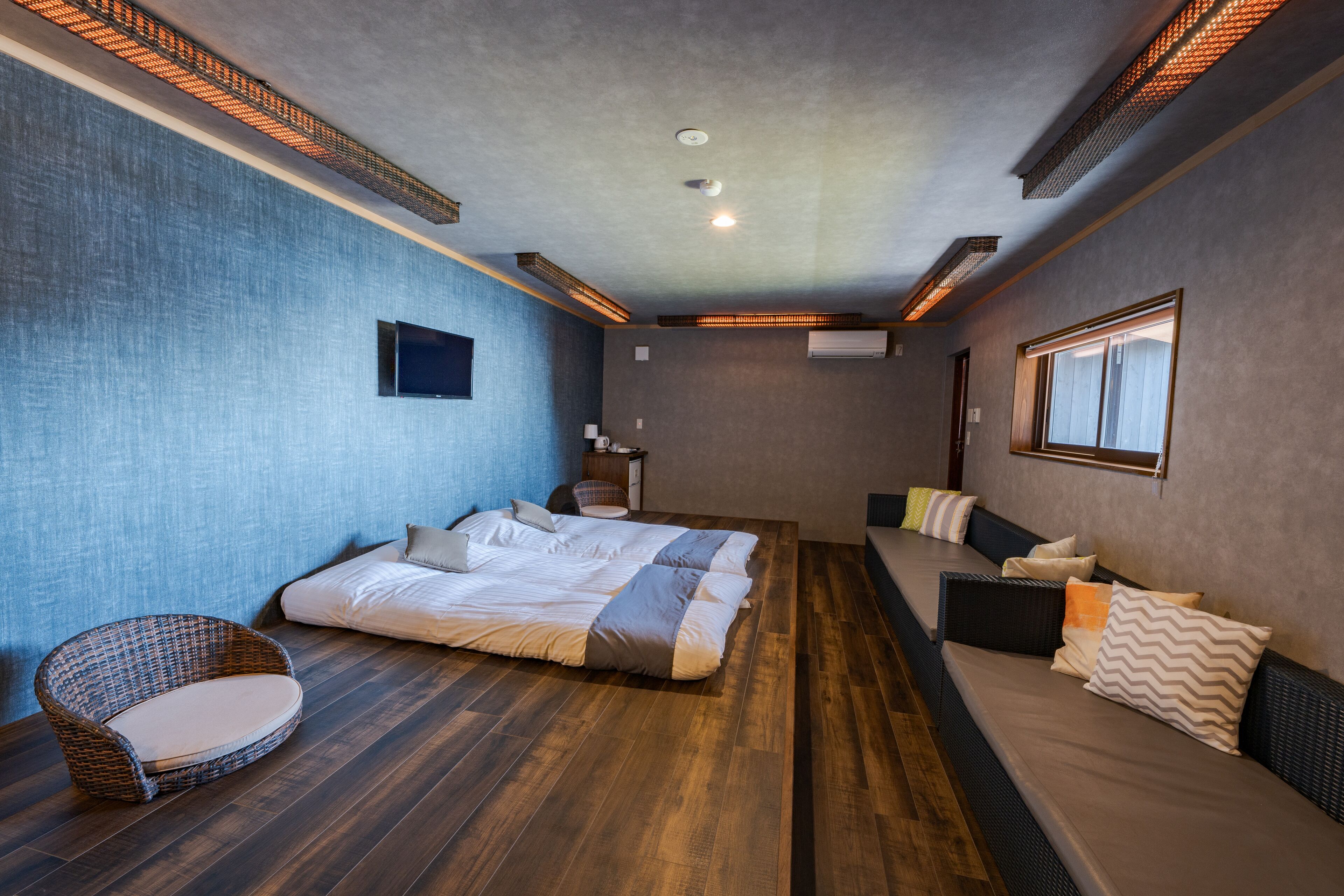 A modern bedroom with a large bed, a wicker chair, and a sofa.