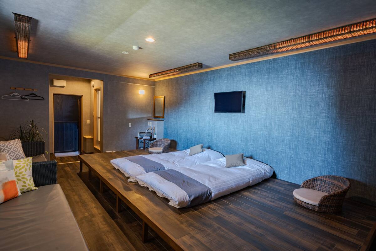 A modern bedroom with a large bed, a bench, a chair, a TV, and a small table.
