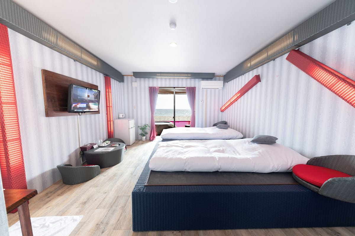 A modern hotel room with a large bed, a TV, a desk, and a view of the sea.