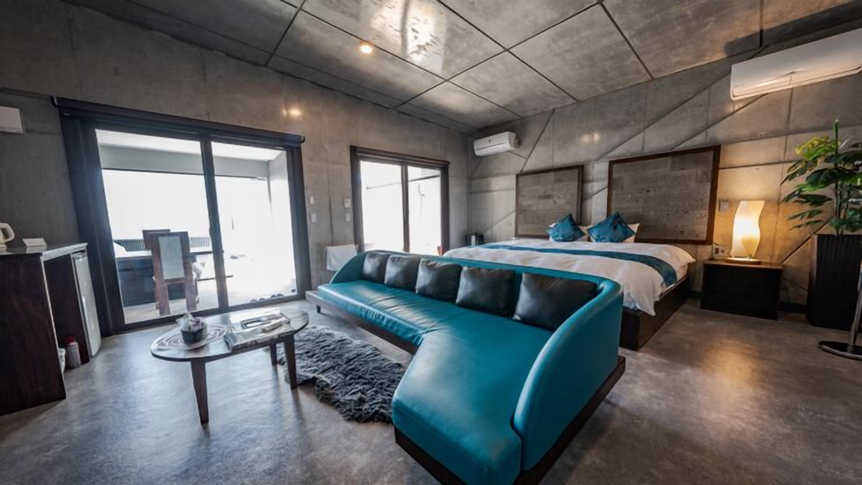 Een moderne hotelkamer met een groot bed, een blauwe bank, een klein tafeltje en een groot raam.