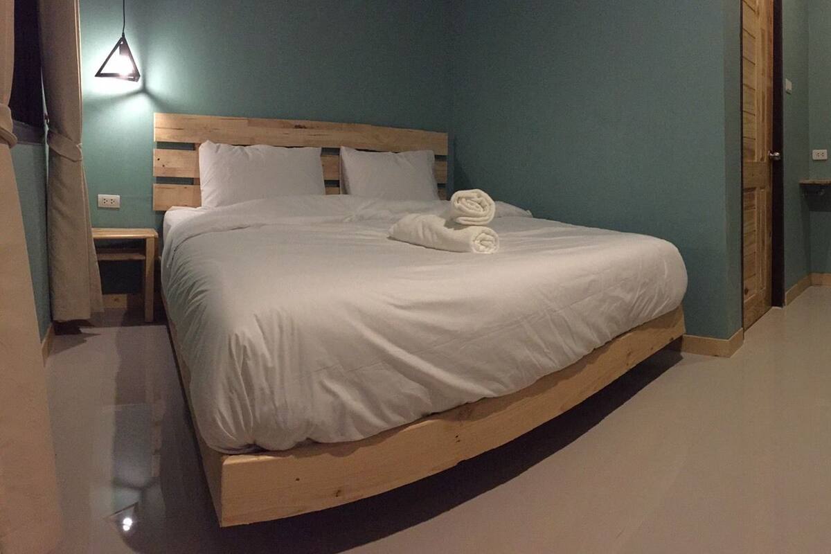 Une chambre à coucher avec un lit en bois, du linge de lit blanc, une petite table de chevet et une commode en bois.