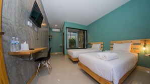 Habitación de hotel con dos camas, un televisor montado en la pared, un escritorio con una silla y una ventana que ofrece vistas a zonas verdes.