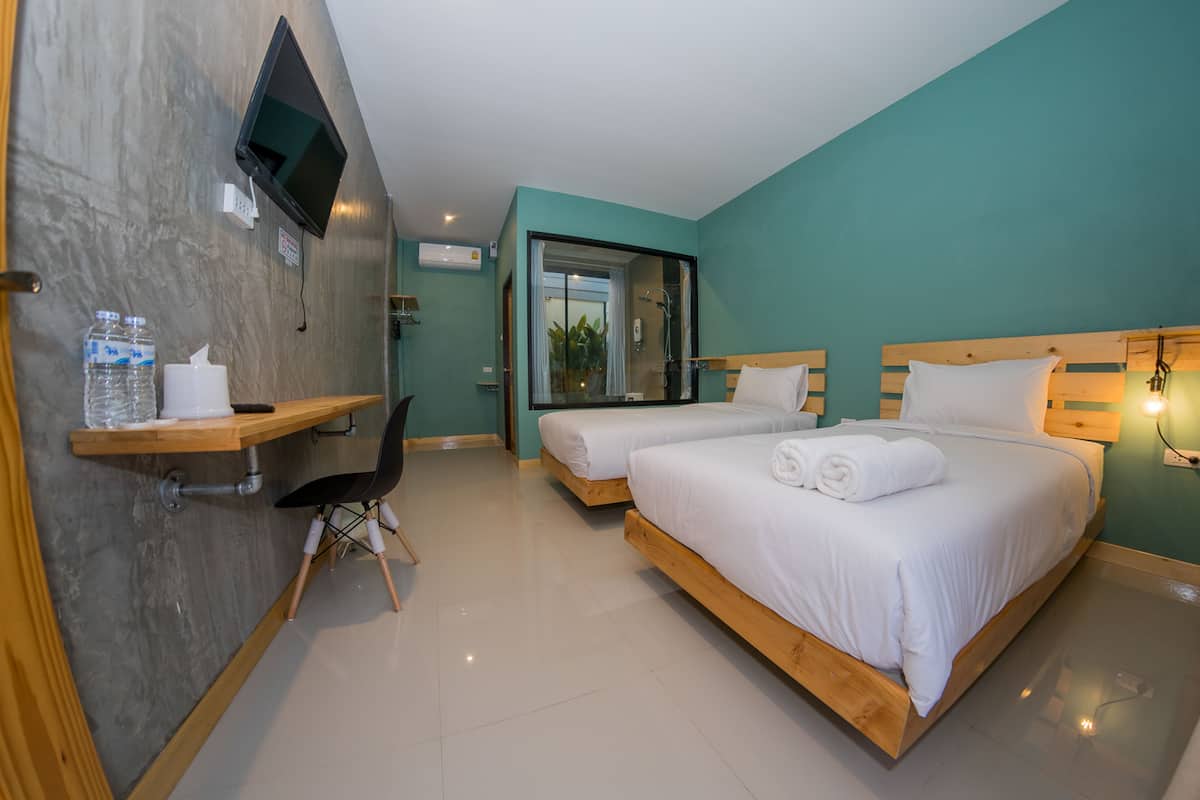 Une chambre d’hôtel avec deux lits, un téléviseur fixé au mur, un bureau avec une chaise et une fenêtre donnant sur un paysage verdoyant.