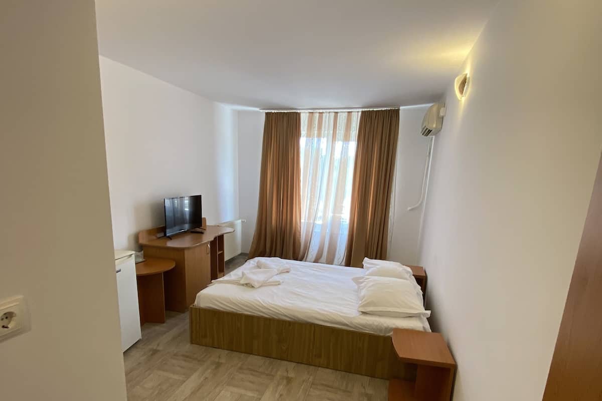 Quarto de hotel com cama, mesas de cabeceira, televisão e janela com cortinas.