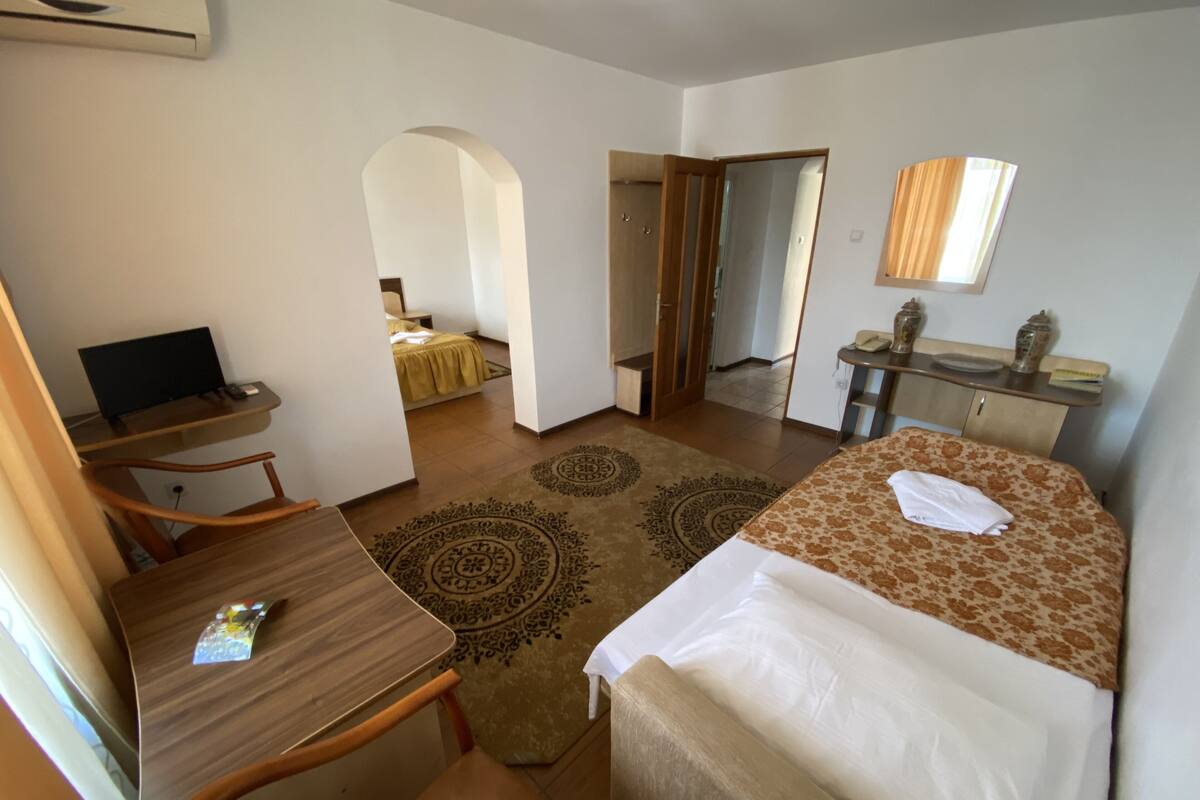 Quarto de hotel com cama, escrivaninha, cadeira, computador, mesinha e espelho.