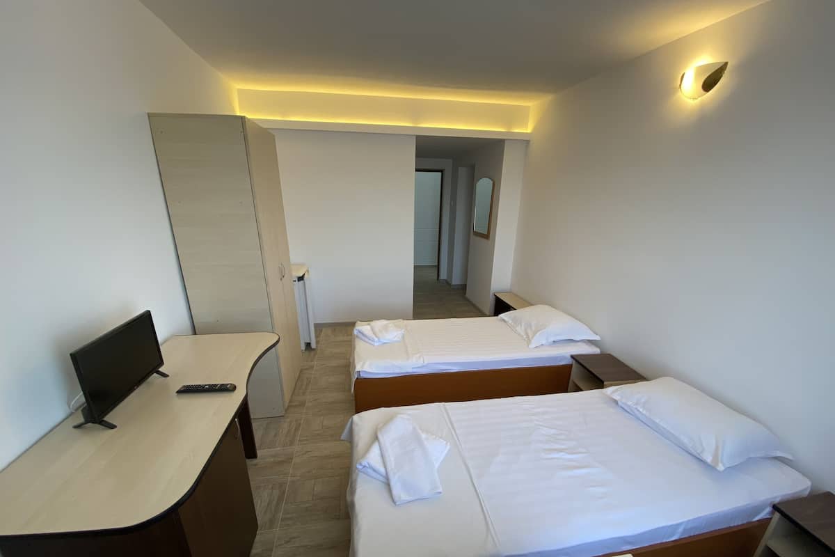 Quarto de hotel com duas camas, uma escrivaninha com computador e um espelho.