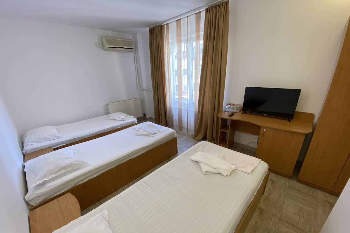 Quarto de hotel com duas camas de solteiro, uma escrivaninha de madeira com televisão e uma janela com cortinas.