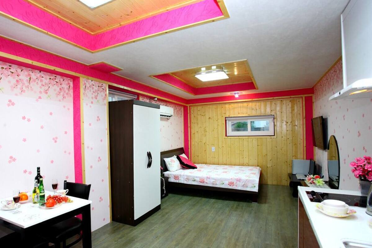 A room with a bed, a desk, a chair, a table with food, and a refrigerator.