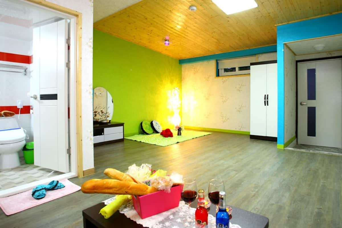 A room with a wooden ceiling, a green wall, a white door, and a table with bread, wine bottles, and a pink box.