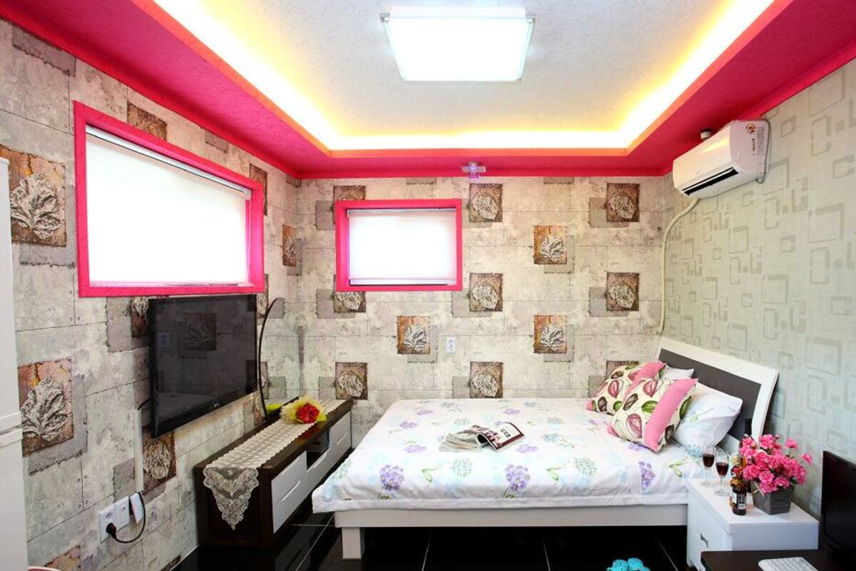 A bedroom with a bed, a TV, a bedside table, and a wall-mounted air conditioner.