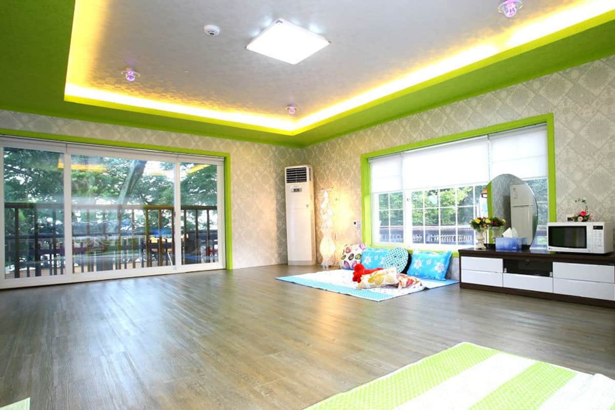 A spacious living room with large windows, a sofa, a coffee table, and a TV stand.