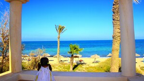 Une vue sur la plage depuis un espace abrité, agrémenté de palmiers et surplombant un ciel bleu azur.