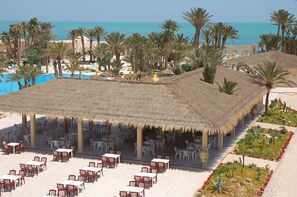 Un complejo turístico frente a la playa con asientos al aire libre, piscina y palmeras.