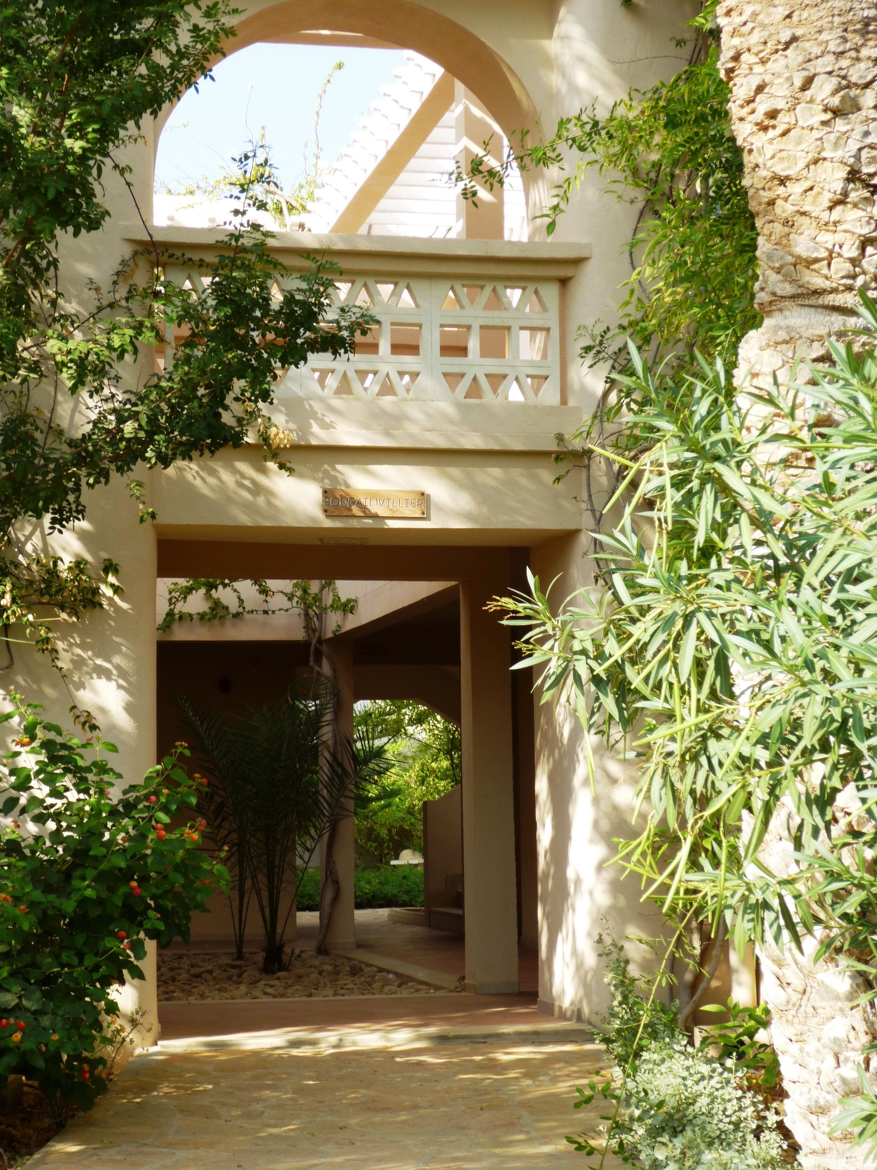 A covered walkway with a sign reading "BOUGATVILLIER" leading to a building entrance.