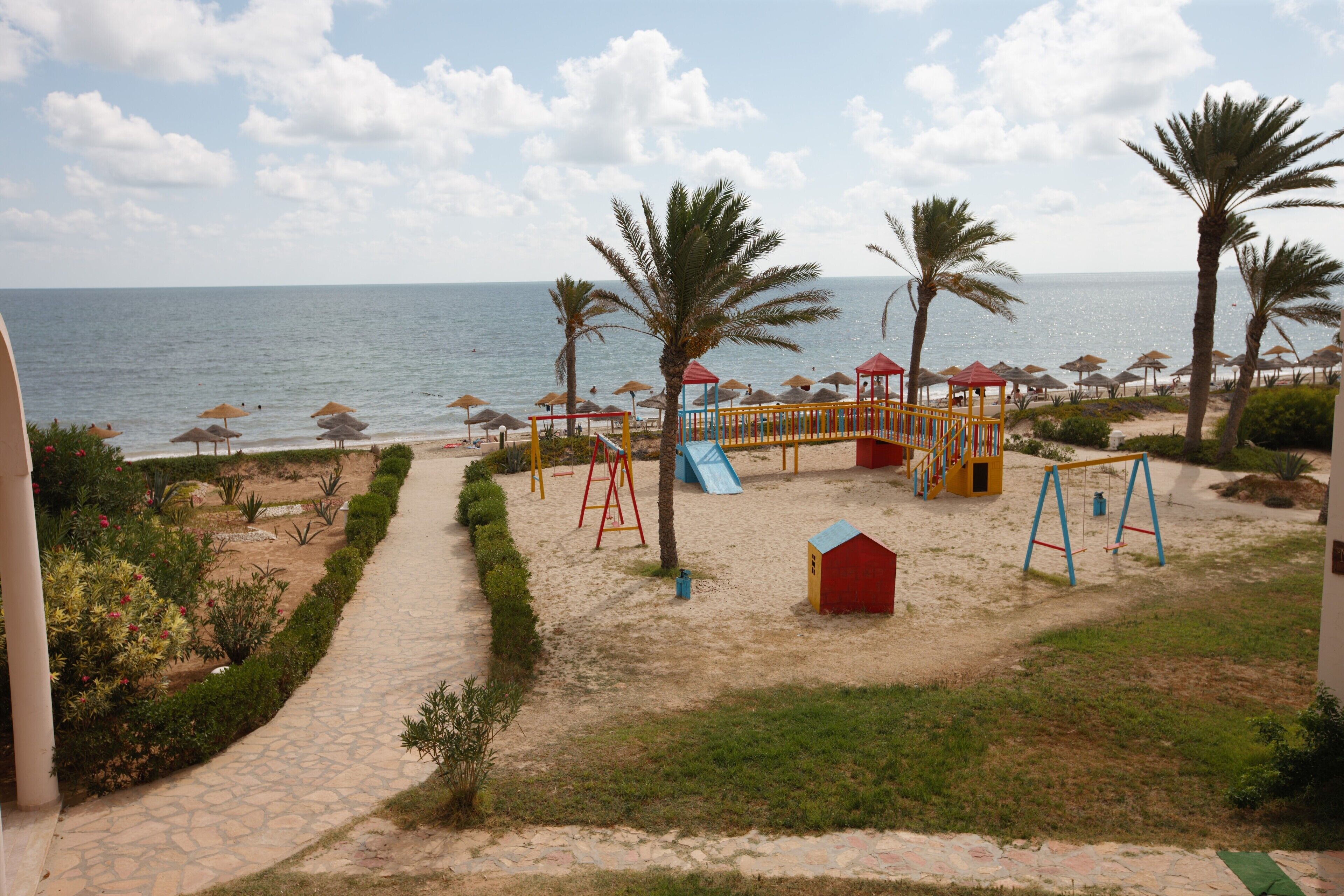 A beachside playground with swings, slides, and a small red building.