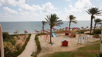 A beachside playground with swings, slides, and a small red building.