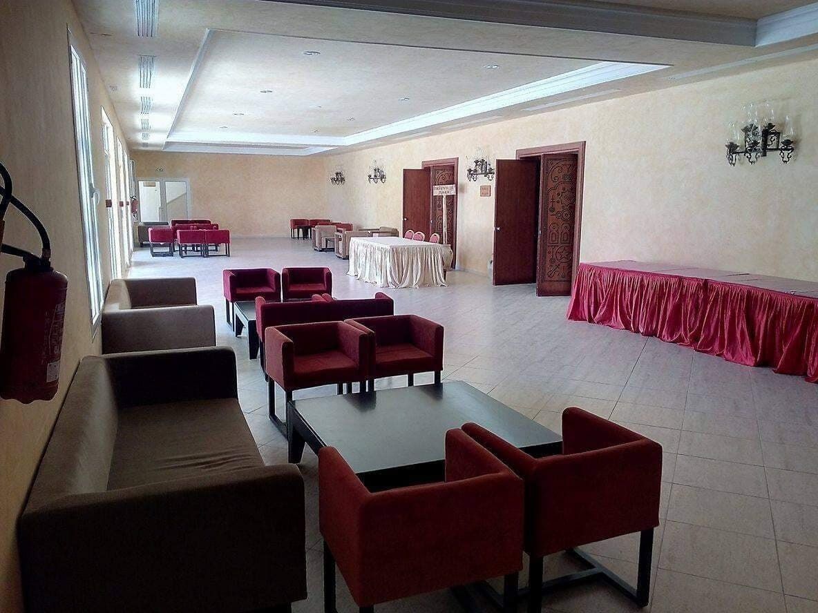 Amplia habitación con varias zonas de estar, incluyendo sillas y mesas rojas, y una mesa tapizada de rojo en el centro.