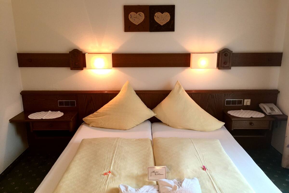 A hotel room with a large bed, two bedside tables, a nightstand with a phone, and wall-mounted lights.