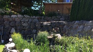 Un jardín con un muro de piedra, un pequeño estanque y un comedero para pájaros.