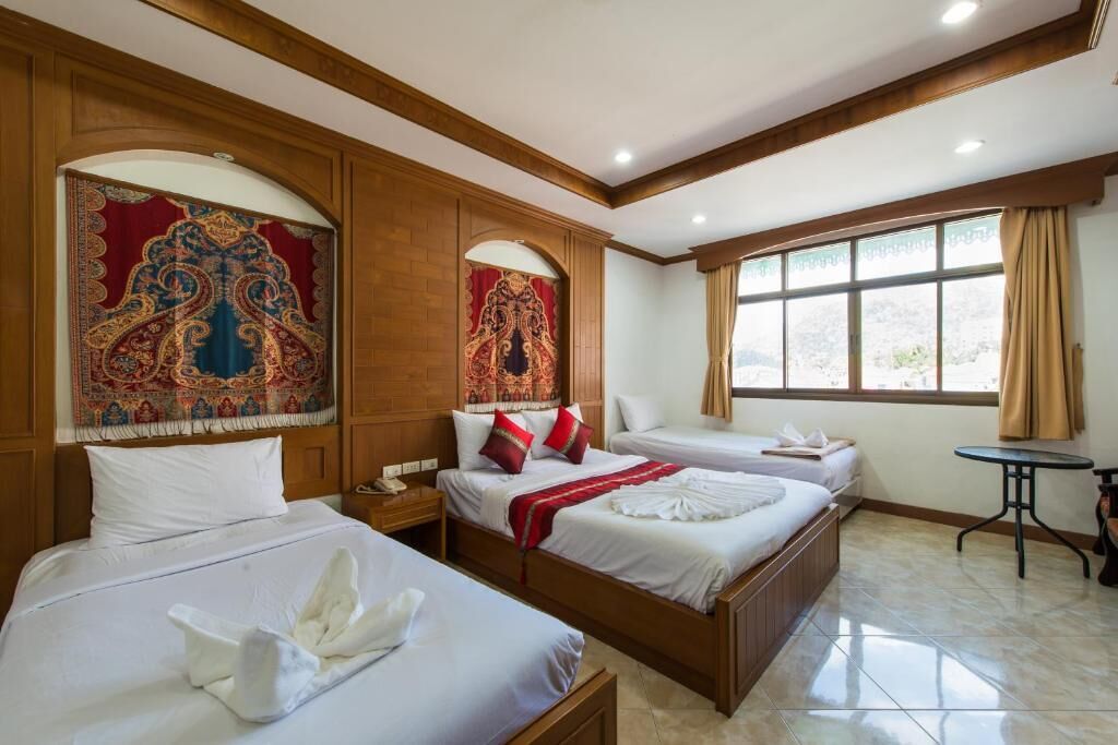 A hotel room with three beds, wooden paneling, and large windows with curtains.