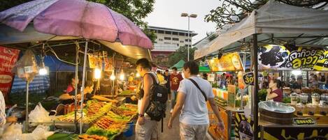 Un mercado callejero animado con varios puestos de comida y un paraguas morado llamativo.