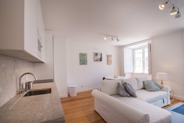 Un salón moderno con un sofá blanco, una mesita y una ventana con luz natural.