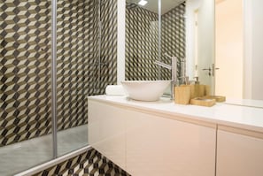 A modern bathroom with a geometric patterned wall, a large mirror, a white sink, and a glass shower enclosure.