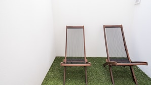 Two wooden chairs with vertical slats, positioned on a patch of artificial grass against a white wall. - Alfama Premium by Homing (Lisbon)