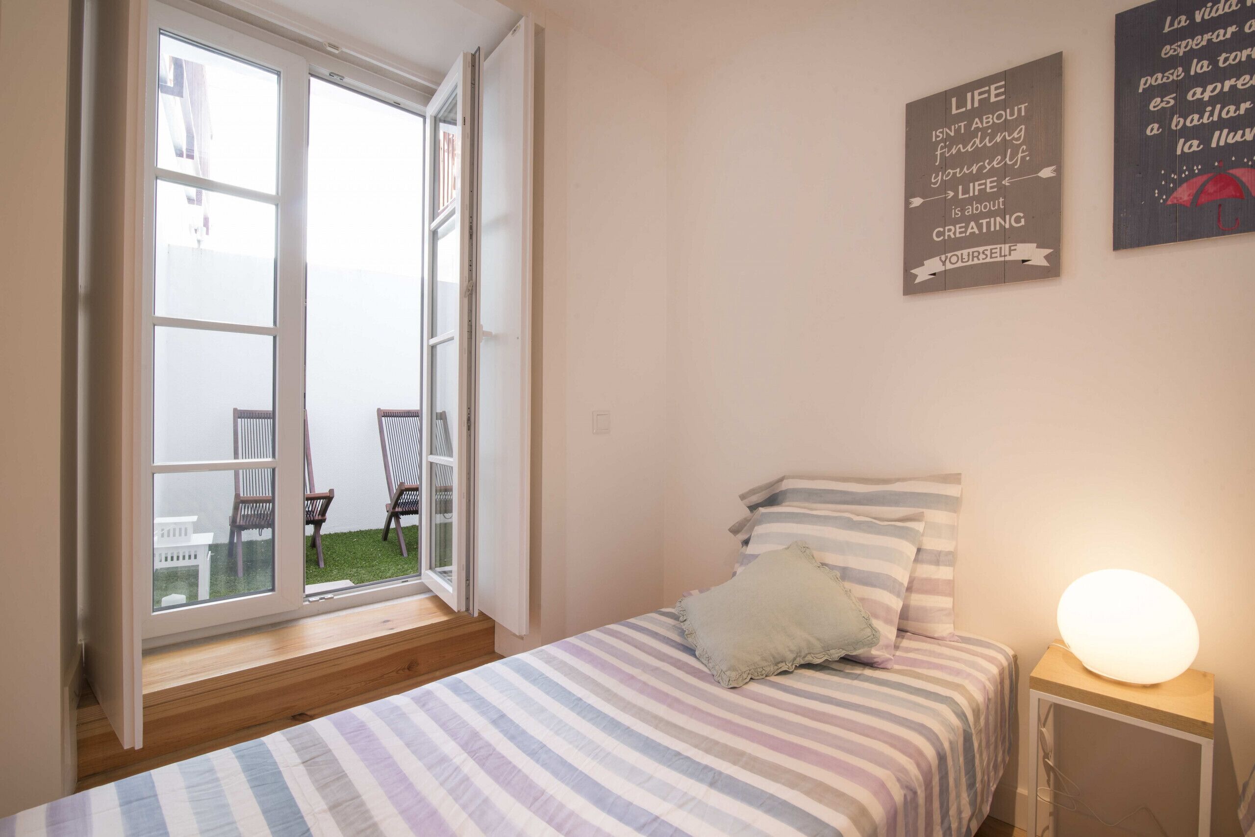 Een slaapkamer met een bed, een bedlampje en een raam met uitzicht op een terras.